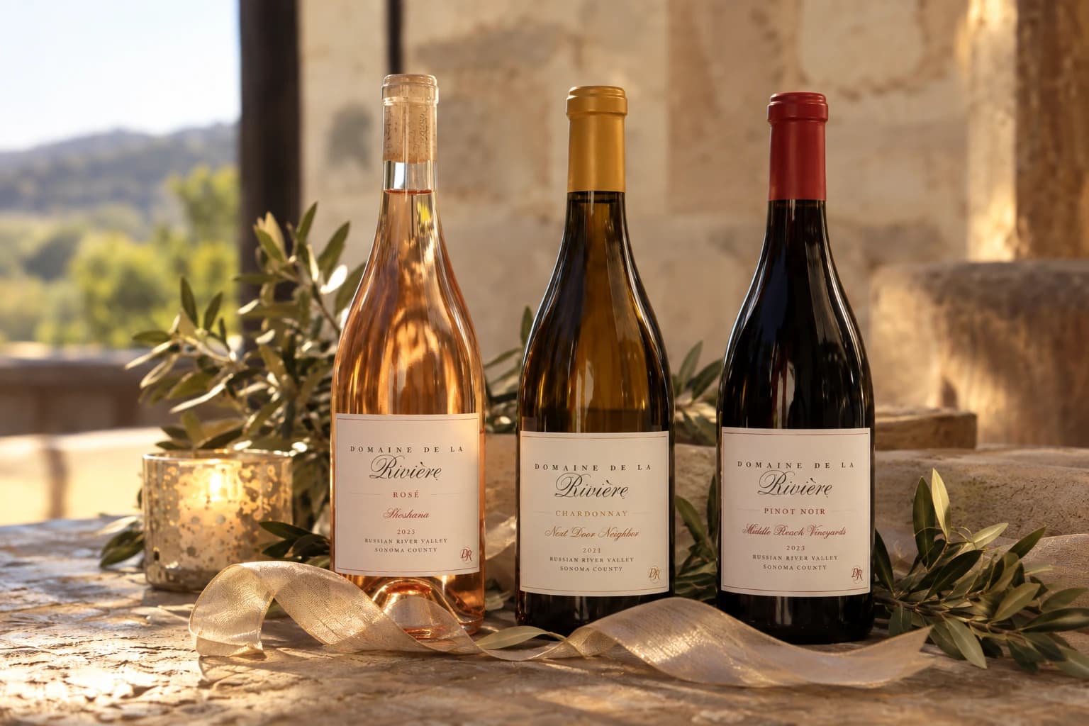 2025 Shoshana Rosé of Pinot Noir, 2021 Next Door Neighbor Chardonnay, and 2021 Middle Reach Vineyards Pinot Noir on a stone ledge in late sun